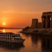 A Nile river cruise ship sailing past ancient Egyptian temple ruins at sunset